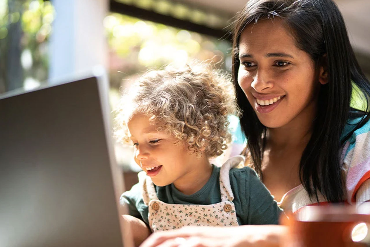 Smiling woman and child with curly hair look at laptop together